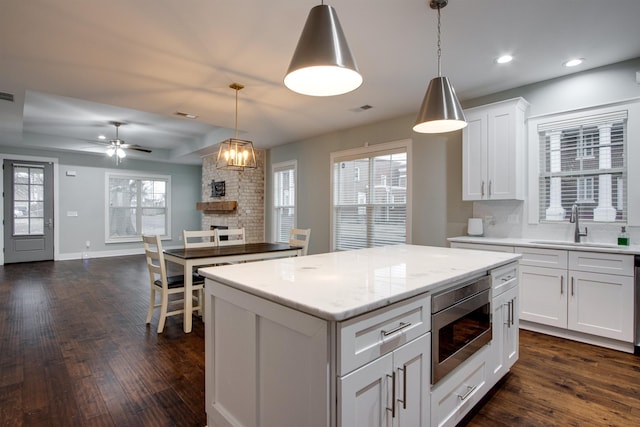 kitchen with a fireplace, built in microwave, white cabinets, a kitchen island, and hanging light fixtures