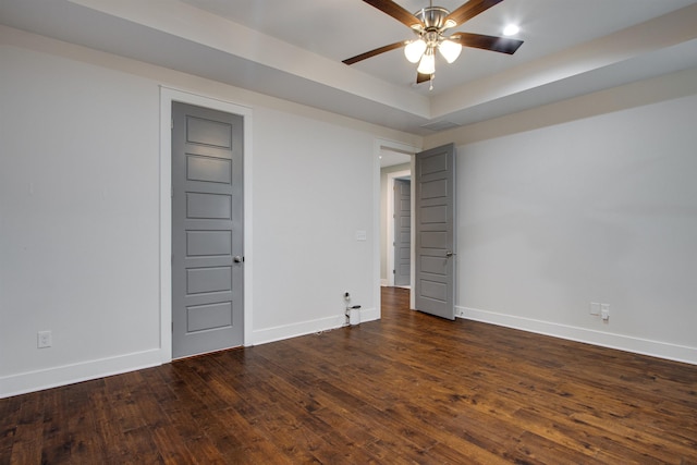 spare room with dark hardwood / wood-style flooring, a raised ceiling, and ceiling fan