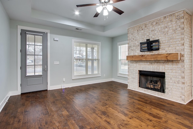 unfurnished living room with a raised ceiling, ceiling fan, dark hardwood / wood-style flooring, and a brick fireplace