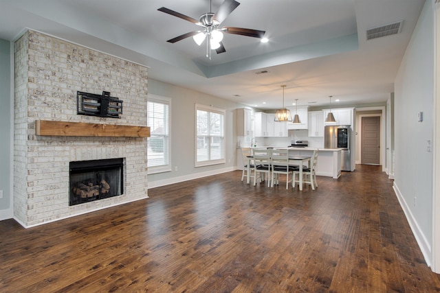 living room with a fireplace, dark hardwood / wood-style flooring, a raised ceiling, and ceiling fan