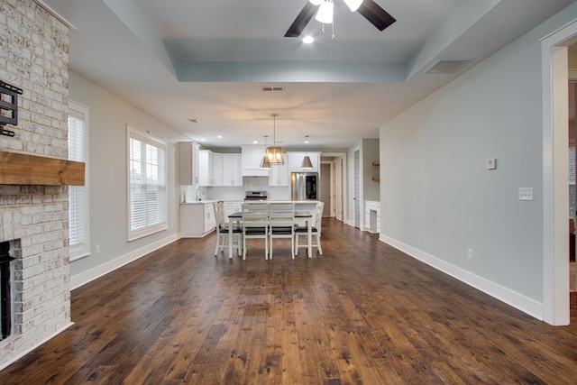 dining space with dark hardwood / wood-style floors, a raised ceiling, and a fireplace