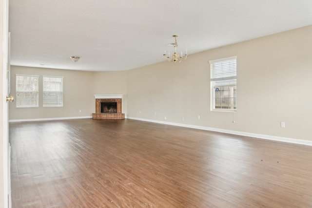 unfurnished living room with a fireplace, hardwood / wood-style floors, an inviting chandelier, and a healthy amount of sunlight