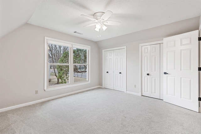 unfurnished bedroom with a textured ceiling, multiple closets, ceiling fan, and vaulted ceiling