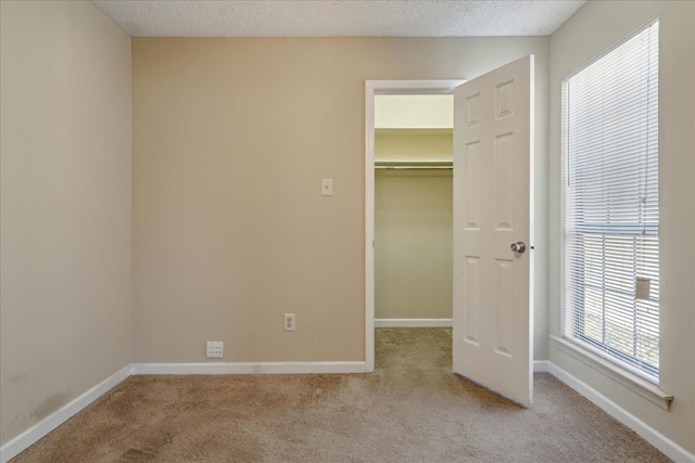 unfurnished bedroom with a textured ceiling, a walk in closet, and light carpet