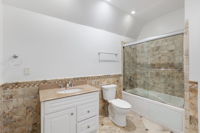 full bathroom featuring vanity, shower / bath combination with glass door, lofted ceiling, toilet, and tile walls