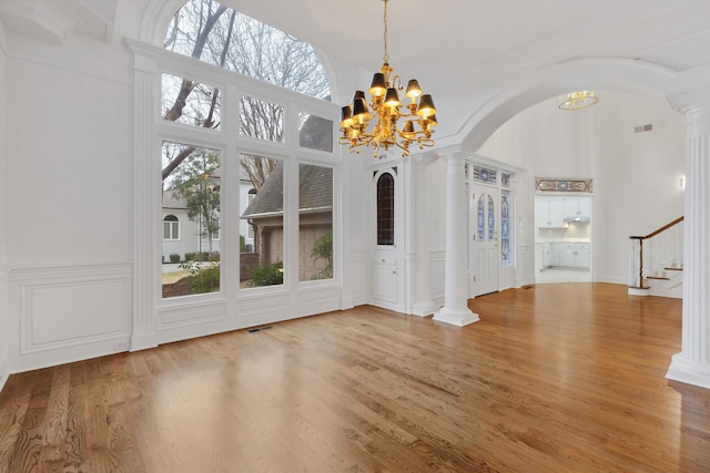 interior space with ornate columns, hardwood / wood-style floors, a healthy amount of sunlight, and an inviting chandelier