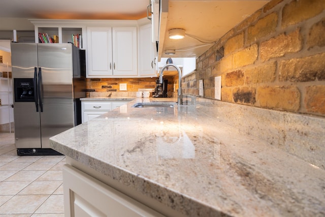 kitchen with white cabinetry, light stone countertops, sink, stainless steel refrigerator with ice dispenser, and light tile patterned floors