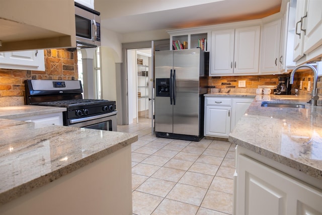 kitchen featuring sink, light tile patterned floors, light stone counters, white cabinets, and appliances with stainless steel finishes