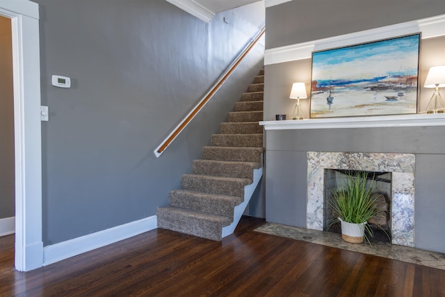 staircase featuring a fireplace, wood-type flooring, and crown molding