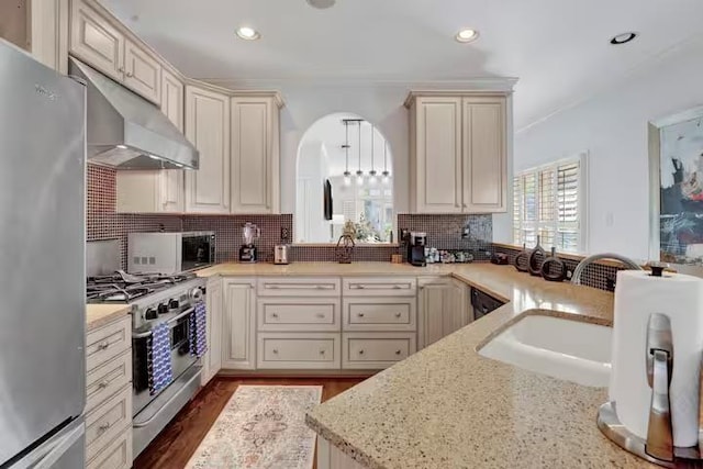 kitchen featuring decorative backsplash, light stone countertops, stainless steel appliances, and cream cabinetry