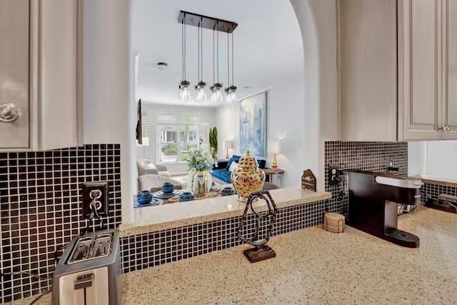 kitchen featuring light stone countertops, backsplash, and hanging light fixtures