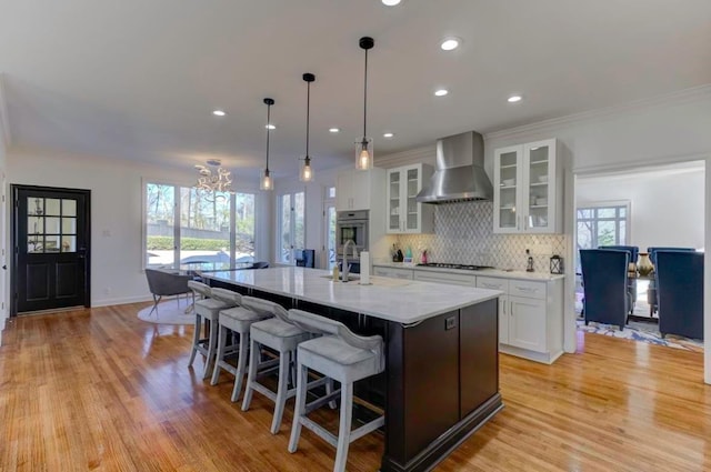 kitchen featuring white cabinetry, wall chimney range hood, gas stovetop, a large island with sink, and a chandelier