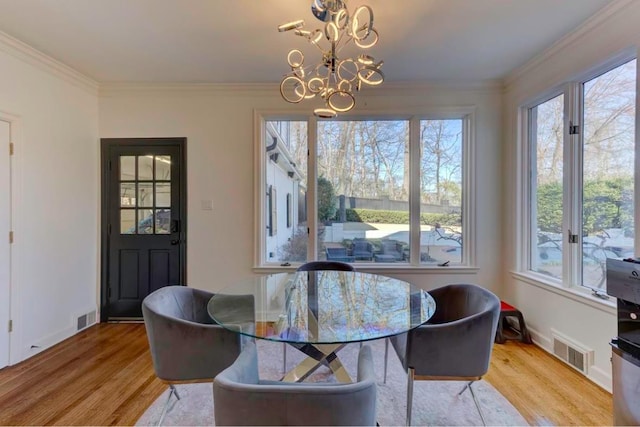 dining room with ornamental molding, light wood-type flooring, and an inviting chandelier