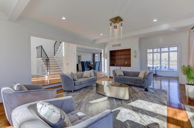 living room featuring hardwood / wood-style flooring, built in features, ornamental molding, beamed ceiling, and a chandelier