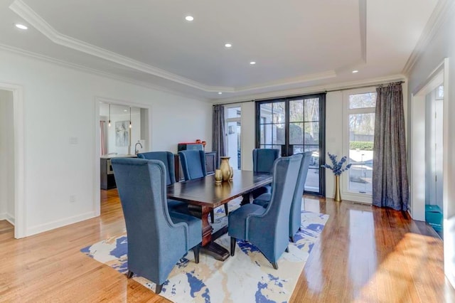 dining space featuring light hardwood / wood-style flooring, a raised ceiling, and crown molding