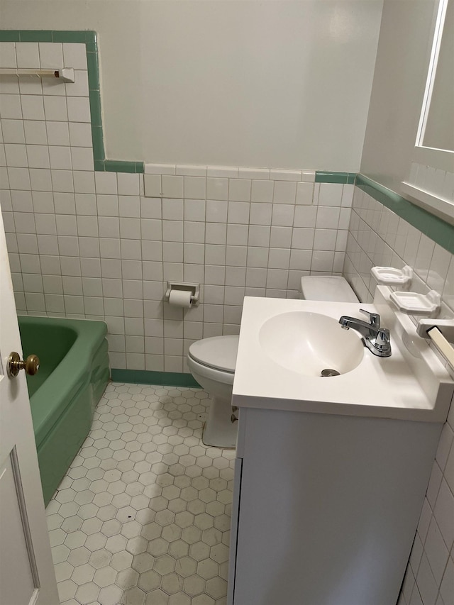 bathroom with toilet, tile patterned flooring, tile walls, a bath, and vanity