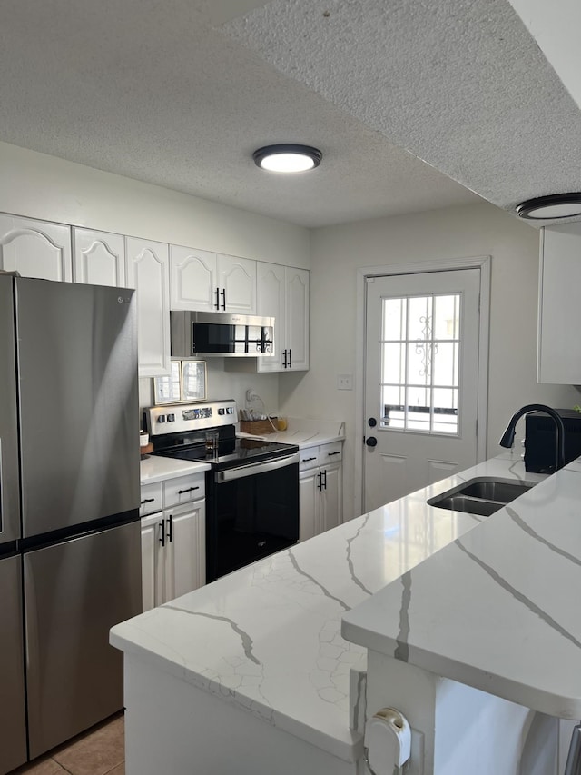 kitchen with stainless steel appliances, light stone countertops, a textured ceiling, white cabinets, and sink