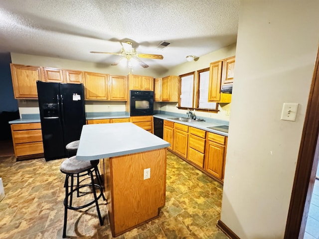 kitchen with sink, a textured ceiling, a kitchen bar, a kitchen island, and black appliances