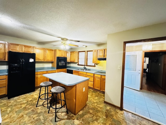 kitchen with black appliances, ceiling fan, a textured ceiling, a kitchen island, and a kitchen bar