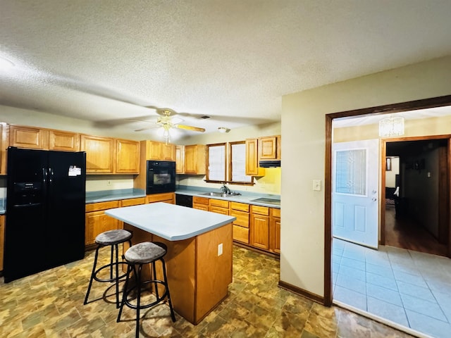 kitchen featuring a center island, black appliances, a kitchen breakfast bar, sink, and a textured ceiling