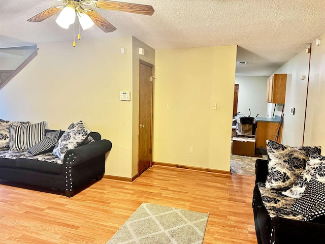 living room featuring ceiling fan, light hardwood / wood-style flooring, and a textured ceiling