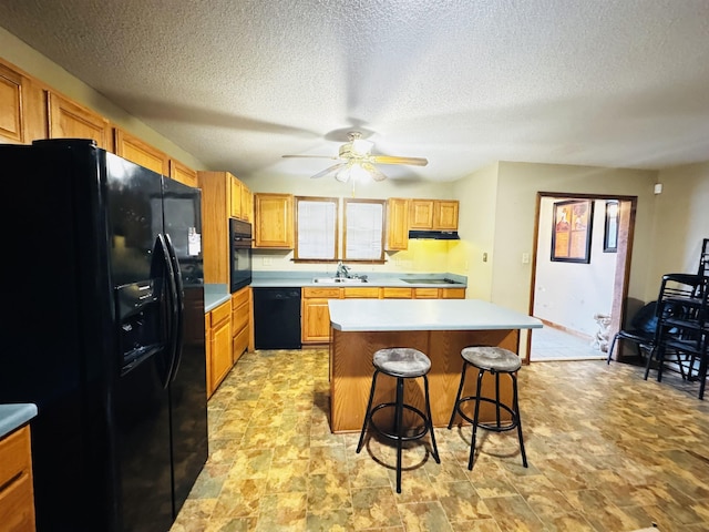 kitchen with ceiling fan, sink, black appliances, a center island, and a breakfast bar area