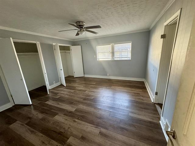 unfurnished bedroom featuring ceiling fan, two closets, a textured ceiling, and dark hardwood / wood-style floors