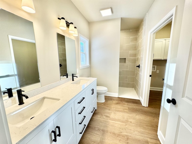 full bathroom featuring a tile shower, wood finished floors, a sink, and toilet