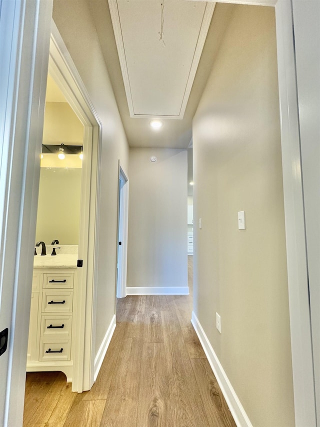 corridor with light wood-style floors, attic access, and baseboards