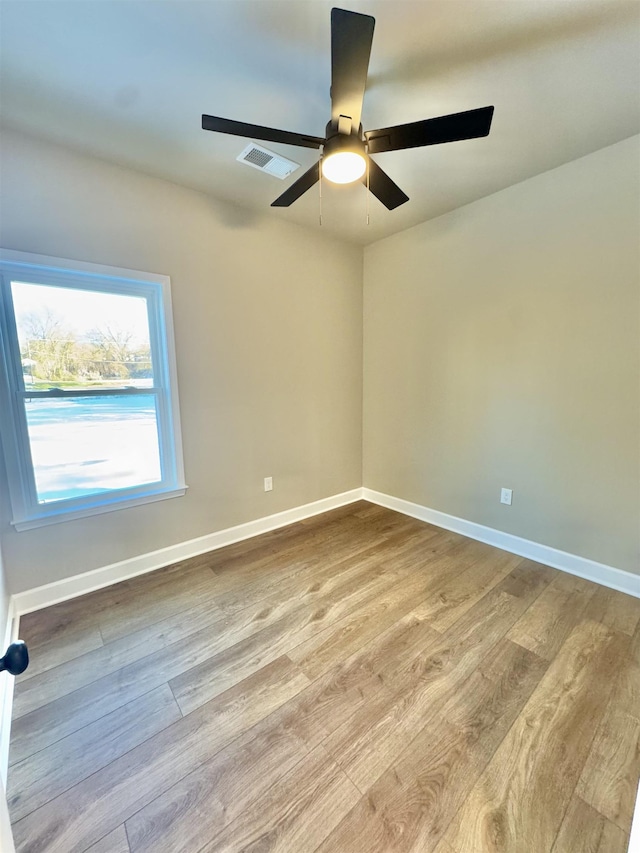 unfurnished room with a ceiling fan, wood finished floors, visible vents, and baseboards