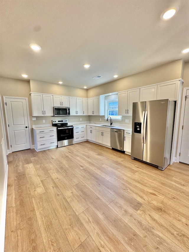 kitchen featuring a sink, white cabinetry, light countertops, appliances with stainless steel finishes, and light wood-type flooring