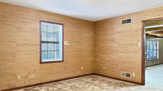 carpeted empty room with wooden walls and a textured ceiling