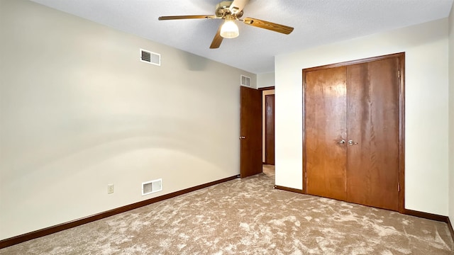 unfurnished bedroom featuring a textured ceiling, light colored carpet, a closet, and ceiling fan