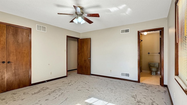 unfurnished bedroom featuring light carpet, a closet, ensuite bathroom, and ceiling fan