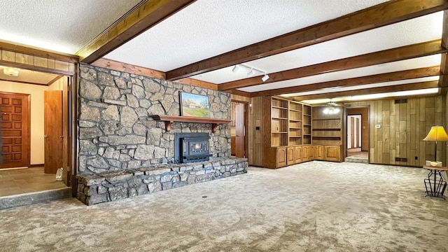 living room with a wood stove, ceiling fan, beamed ceiling, wood walls, and carpet