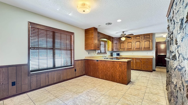 kitchen featuring ceiling fan, wood walls, plenty of natural light, and kitchen peninsula