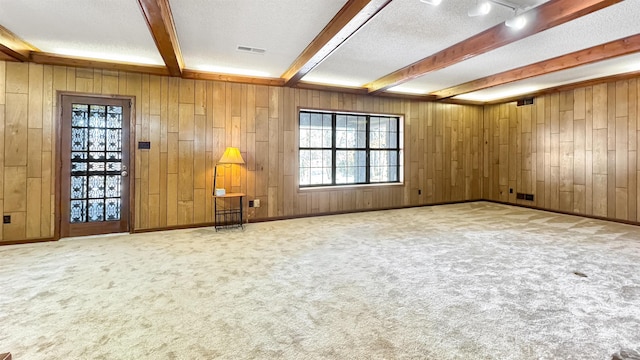 carpeted empty room with a textured ceiling, rail lighting, wood walls, and beam ceiling