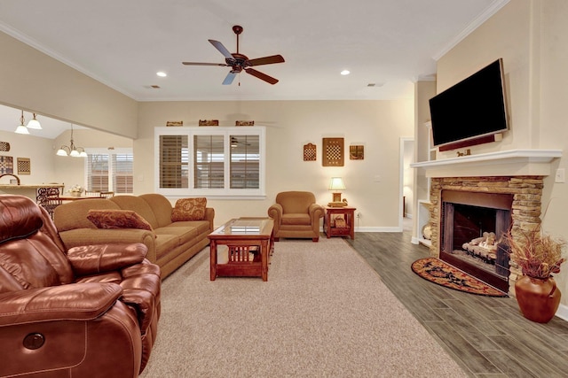 living room featuring hardwood / wood-style flooring, ceiling fan with notable chandelier, ornamental molding, and a fireplace