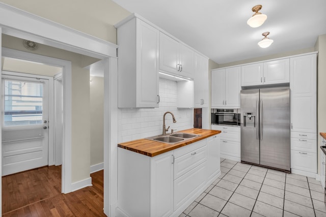 kitchen with appliances with stainless steel finishes, white cabinetry, butcher block countertops, and sink