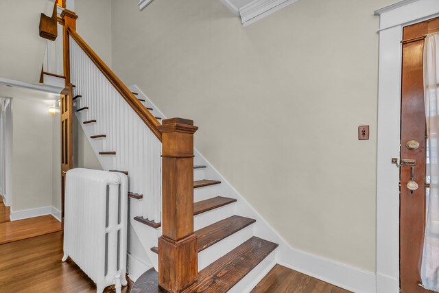 stairway with hardwood / wood-style floors, radiator, and crown molding