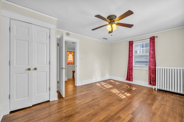 interior space featuring a closet, wood-type flooring, crown molding, ceiling fan, and radiator heating unit