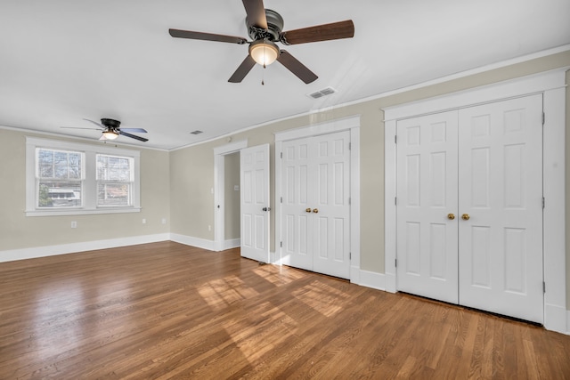 unfurnished bedroom featuring multiple closets, ceiling fan, ornamental molding, and hardwood / wood-style flooring