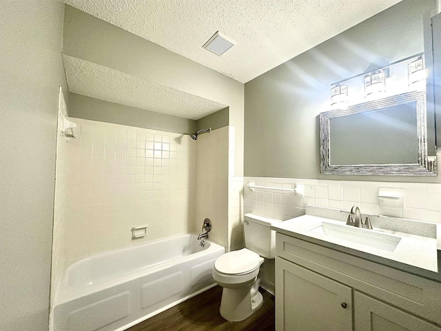 full bathroom with toilet, hardwood / wood-style flooring, a textured ceiling, tile walls, and tiled shower / bath combo