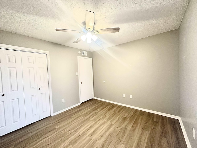 unfurnished bedroom featuring a textured ceiling, wood-type flooring, ceiling fan, and a closet