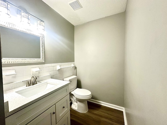 bathroom featuring a textured ceiling, tile walls, hardwood / wood-style floors, toilet, and vanity