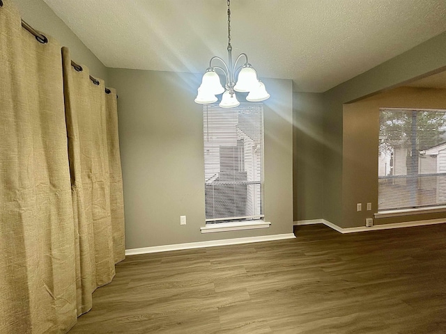 unfurnished dining area featuring a wealth of natural light, an inviting chandelier, a textured ceiling, and wood-type flooring