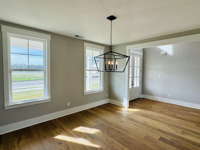 unfurnished dining area with an inviting chandelier and hardwood / wood-style flooring