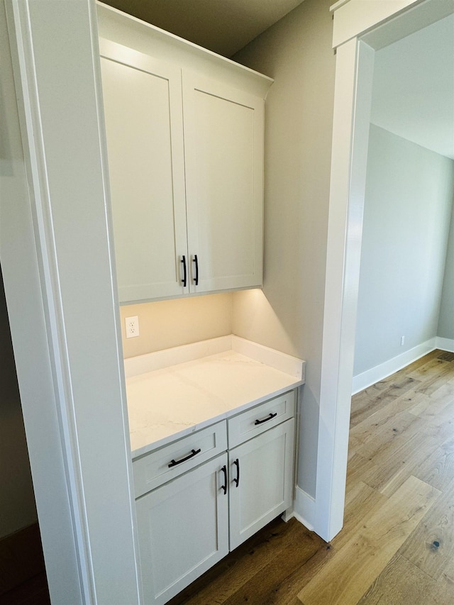 bar featuring white cabinets, light hardwood / wood-style floors, and light stone counters