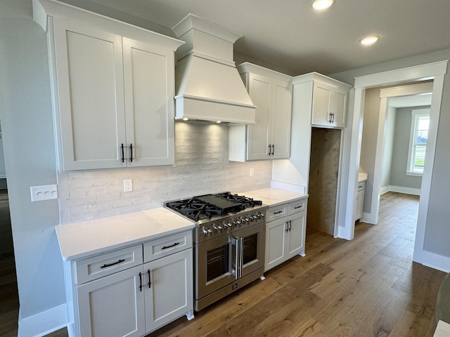 kitchen featuring high end stainless steel range oven, custom range hood, white cabinetry, and tasteful backsplash