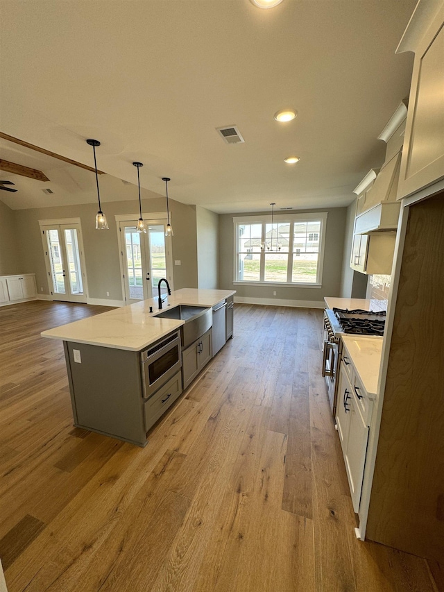 kitchen featuring sink, stainless steel appliances, french doors, a center island with sink, and pendant lighting